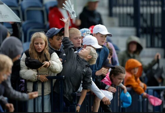 کودکان حاضر در سکوهای تماشاگران پشت منطقه سبزِ سوراخ هجدهم تلاش می‌کنند توپ‌هایی را که بازیکنان پس از پایان بازی برایشان پرتاب می‌کنند، بگیرند، اما به جای آن یک دستکش گلف می‌گیرند.